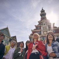 Menschen stehen lachend vor einem historischen Rathaus mit Uhrturm. Die Sonne scheint hell am Himmel., © Esslinger Stadtmarketing &amp; Tourismus GmbH