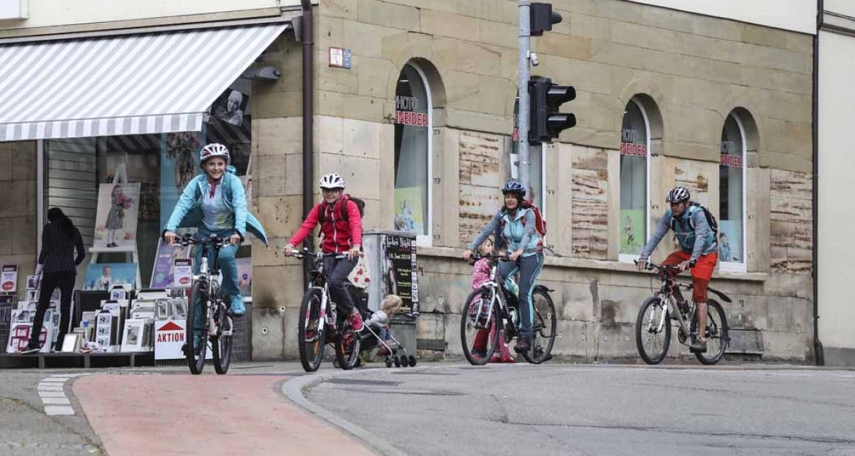 Eine Gruppe von Radfahrern, darunter Kinder, fährt durch die Kirchheimer Innenstadt. Sie tragen Helme und sind auf einem Radweg unterwegs., © Schwäbische Alb Tourismusverband e.V. Eine Gruppe von Radfahrern, darunter Kinder, fährt durch die Kirchheimer Innenstadt. Sie tragen Helme und sind auf einem Radweg unterwegs., © Schwäbische Alb Tourismusverband e.V.