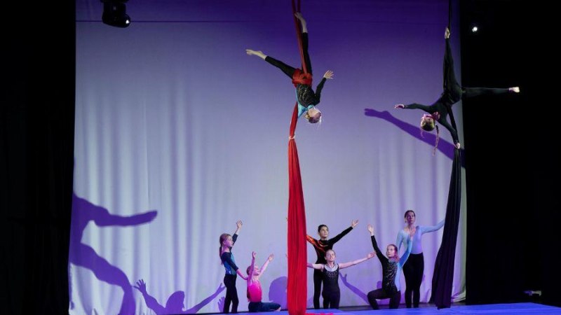 Kinder zeigen Luftakrobatik an roten und schwarzen T&uuml;chern auf einer B&uuml;hne. Einige stehen auf Matten, w&auml;hrend andere in der Luft h&auml;ngen., &copy; Kunstschule Labyrinth