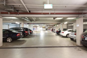 Tiefgarage mit geparkten Autos auf beiden Seiten, helle Beleuchtung und sichtbare Rohrleitungen an der Decke., © PLAZA INN Rieker Stuttgart Hauptbahnhof Tiefgarage mit geparkten Autos auf beiden Seiten, helle Beleuchtung und sichtbare Rohrleitungen an der Decke., © PLAZA INN Rieker Stuttgart Hauptbahnhof