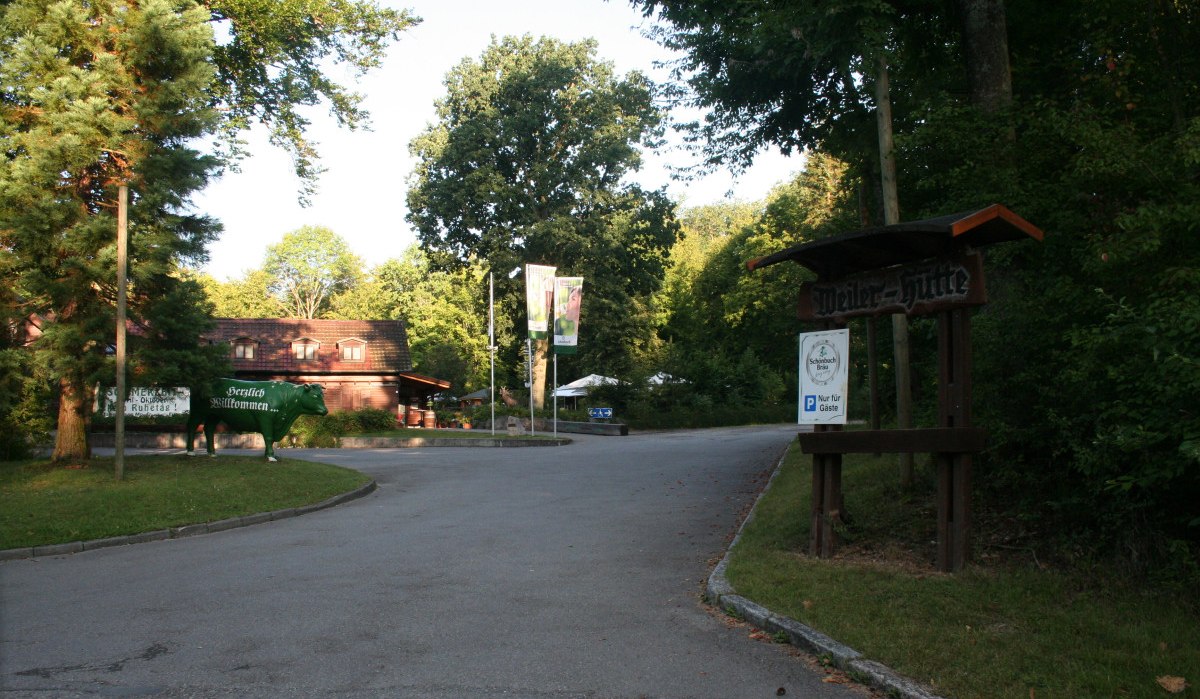 Eingang zur Weiler Hütte mit einem Schild und einer grünen Kuhfigur. Umgeben von Bäumen und einem Parkplatzschild für Gäste., © Natur.Nah. Schönbuch & Heckengäu Eingang zur Weiler Hütte mit einem Schild und einer grünen Kuhfigur. Umgeben von Bäumen und einem Parkplatzschild für Gäste., © Natur.Nah. Schönbuch & Heckengäu