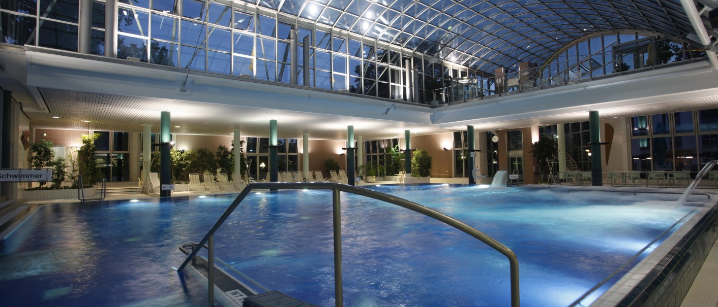 Beleuchtetes Schwimmbad mit Glasdach und Pflanzen. Der Pool ist von Liegestühlen umgeben, die Atmosphäre ist ruhig und entspannend., © Stuttgarter Bäder Beleuchtetes Schwimmbad mit Glasdach und Pflanzen. Der Pool ist von Liegestühlen umgeben, die Atmosphäre ist ruhig und entspannend., © Stuttgarter Bäder