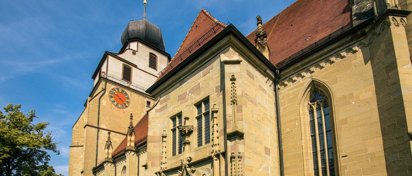 Die Stiftskirche Herrenberg mit ihrem markanten Uhrturm und gotischen Fenstern strahlt im Sonnenlicht vor blauem Himmel., © Stuttgart-Marketing GmbH, Sarah Schmid