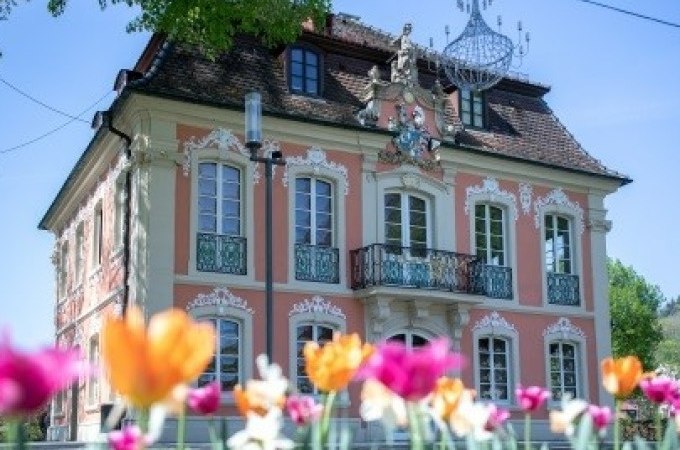 Ein barockes Geb&auml;ude mit verzierten Fenstern und Balkon, umgeben von bunten Tulpen im Vordergrund. Ein Kronleuchter h&auml;ngt im Freien., &copy; Touristik und Marketing GmbH