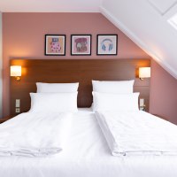 Ein stilvoll eingerichtetes Hotelzimmer mit einem gro&szlig;en Doppelbett, wei&szlig;en Bettlaken und Kissen. Drei Bilder schm&uuml;cken die Wand &uuml;ber dem Bett., &copy; Novum  Hospitality
