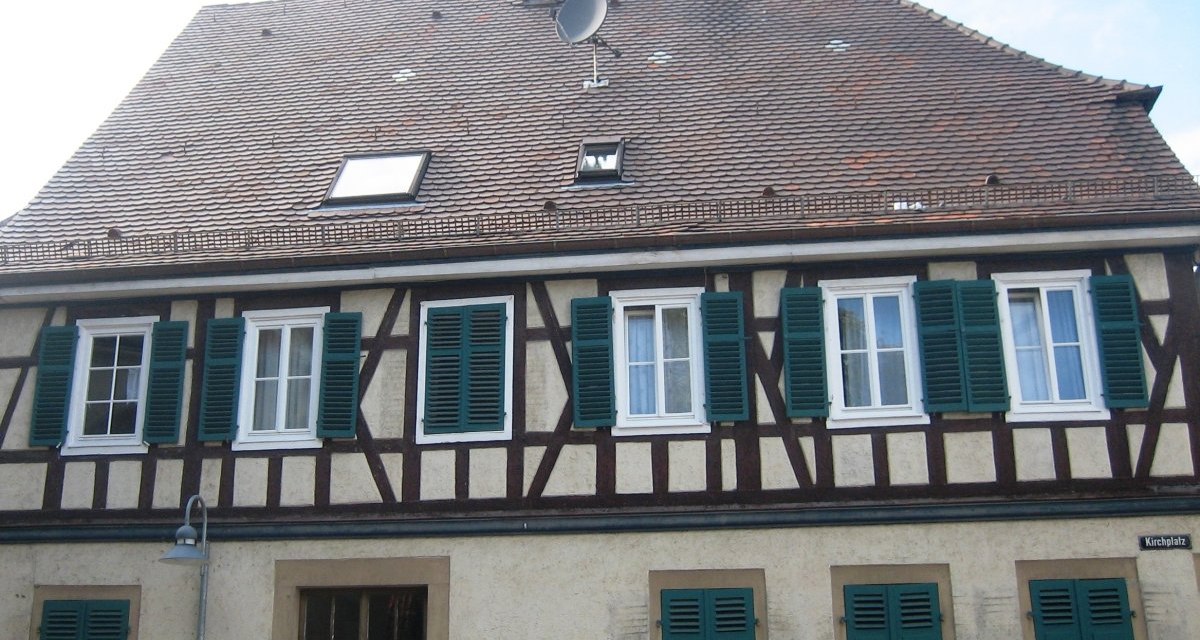 Fachwerkhaus mit grünen Fensterläden, Ziegeldach und Satellitenschüssel. Schild mit der Aufschrift 'Kirchplatz' an der Wand., © Land der 1000 Hügel - Kraichgau-Stromberg Fachwerkhaus mit grünen Fensterläden, Ziegeldach und Satellitenschüssel. Schild mit der Aufschrift 'Kirchplatz' an der Wand., © Land der 1000 Hügel - Kraichgau-Stromberg