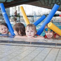 Vier Kinder im Schwimmbad lehnen am Beckenrand und halten bunte Schwimmnudeln. Sie lächeln und tragen Badeanzüge., © Badezentrum Sindelfingen Vier Kinder im Schwimmbad lehnen am Beckenrand und halten bunte Schwimmnudeln. Sie lächeln und tragen Badeanzüge., © Badezentrum Sindelfingen