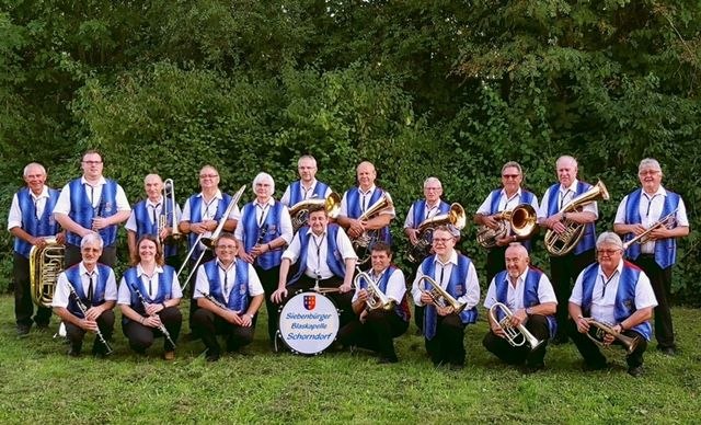 Eine Blaskapelle in blauen Westen posiert im Freien mit Instrumenten vor einer grünen Hecke., © Siebenbürgen Blaskapelle Schorndorf Eine Blaskapelle in blauen Westen posiert im Freien mit Instrumenten vor einer grünen Hecke., © Siebenbürgen Blaskapelle Schorndorf