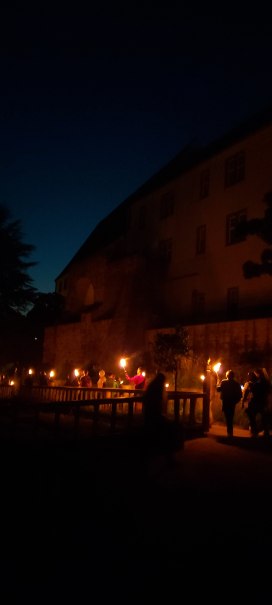 Eine Gruppe von Menschen h&auml;lt Fackeln bei Nacht vor einem historischen Geb&auml;ude. Der Himmel ist dunkelblau, und die Szene wirkt geheimnisvoll., &copy; Stadtmarketing Leonberg