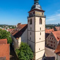 Die Evangelische Stadtkirche Bietigheim-Bissingen ragt über die roten Dächer der Altstadt, umgeben von Bäumen und unter einem klaren blauen Himmel., © SMG, Achim Mende Die Evangelische Stadtkirche Bietigheim-Bissingen ragt über die roten Dächer der Altstadt, umgeben von Bäumen und unter einem klaren blauen Himmel., © SMG, Achim Mende