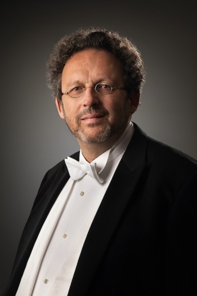 Ein Mann im Smoking mit Fliege und Brille posiert vor einem dunklen Hintergrund. Er hat lockiges Haar und einen gepflegten Bart., © Schwarzwald Musikfestival gGmbH