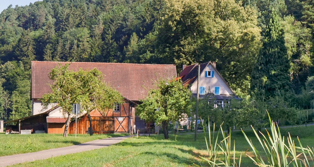 Ein Bauernhof mit Scheune und Wohnhaus, umgeben von Bäumen und Wiesen, vor einem bewaldeten Hügel., © Natur.Nah. Schönbuch & Heckengäu Ein Bauernhof mit Scheune und Wohnhaus, umgeben von Bäumen und Wiesen, vor einem bewaldeten Hügel., © Natur.Nah. Schönbuch & Heckengäu
