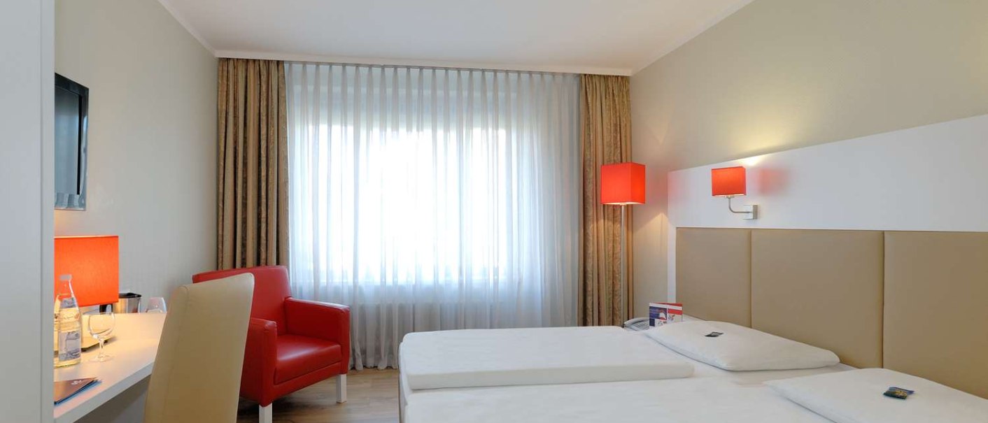 Modernes Hotelzimmer mit zwei Einzelbetten, rotem Sessel, Schreibtisch und Fenster mit Vorhängen. Rote Lampen sorgen für Akzente., © Hotel Stuttgart-Sindelfingen City by Tulip Inn Modernes Hotelzimmer mit zwei Einzelbetten, rotem Sessel, Schreibtisch und Fenster mit Vorhängen. Rote Lampen sorgen für Akzente., © Hotel Stuttgart-Sindelfingen City by Tulip Inn