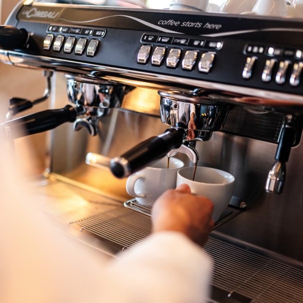 Espressomaschine gießt Kaffee in zwei Tassen. Eine Hand hält eine Tasse. Beschriftung: "coffee starts here"., © Mercedes-Benz AG