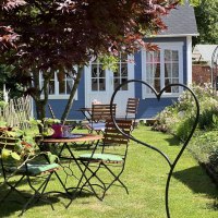 Garten mit Holztischen und -stühlen, umgeben von Pflanzen. Im Hintergrund ein blaues Häuschen und ein Baum mit roten Blättern., © Café Plätschwiesle Garten mit Holztischen und -stühlen, umgeben von Pflanzen. Im Hintergrund ein blaues Häuschen und ein Baum mit roten Blättern., © Café Plätschwiesle