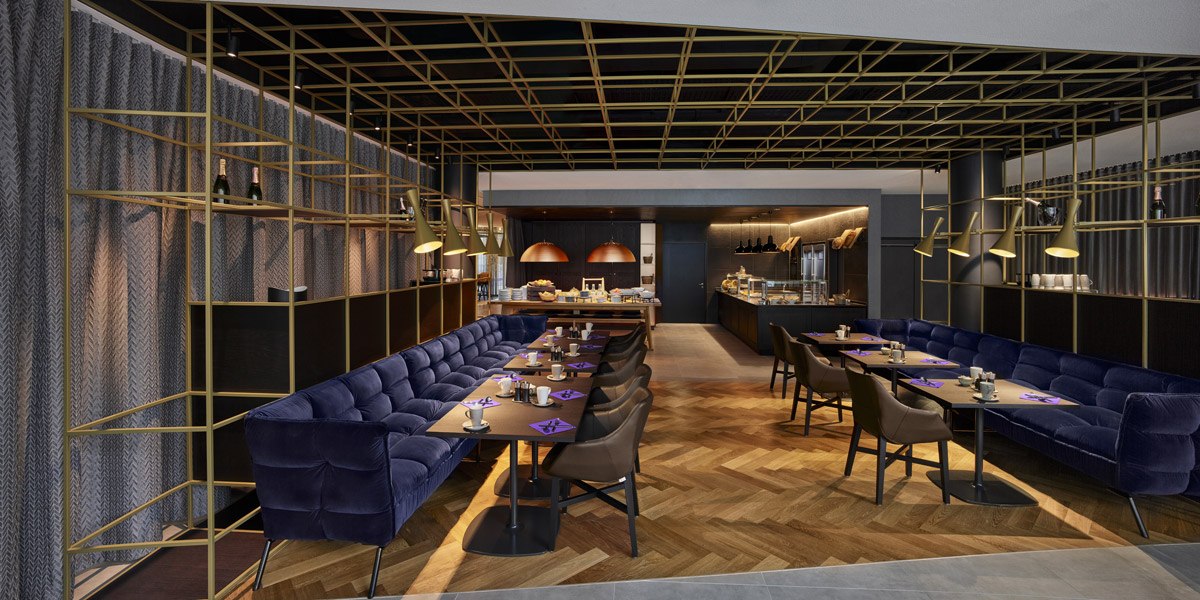 Elegantes Restaurant mit blauen Sofas, Holzboden und goldenen Lampen. Offene Küche im Hintergrund, stilvolle Atmosphäre., © Jaz Hotel Stuttgart