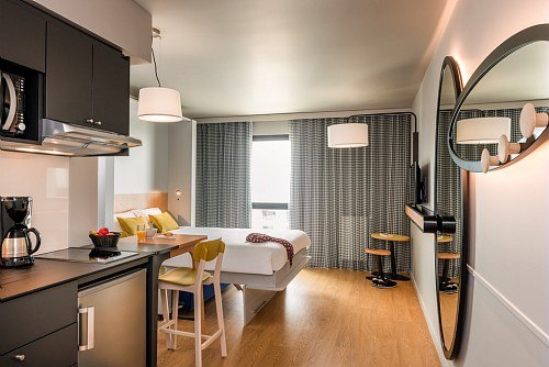 Modernes Studio mit Küchenzeile, Esstisch und Bett. Große Spiegel und Fenster, helle Einrichtung mit Holzboden und stilvollen Möbeln., © adagio access Stuttgart Airport Messe