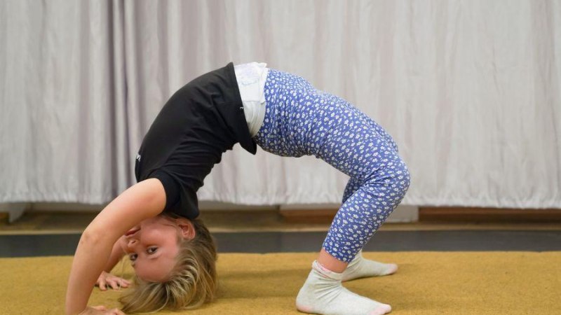 Ein Kind in blauer Leggings und schwarzem Shirt macht eine Brücke auf einem Teppichboden vor einem Vorhang., © Kunstschule Labyrinth Ein Kind in blauer Leggings und schwarzem Shirt macht eine Brücke auf einem Teppichboden vor einem Vorhang., © Kunstschule Labyrinth