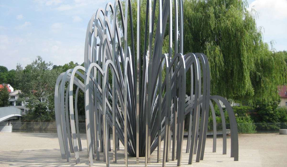 Moderne Skulptur aus gebogenen Metallstreben, die in einem Pavillon-ähnlichen Muster angeordnet sind, umgeben von Bäumen und einem klaren Himmel., © Remstal Tourismus e.V.
