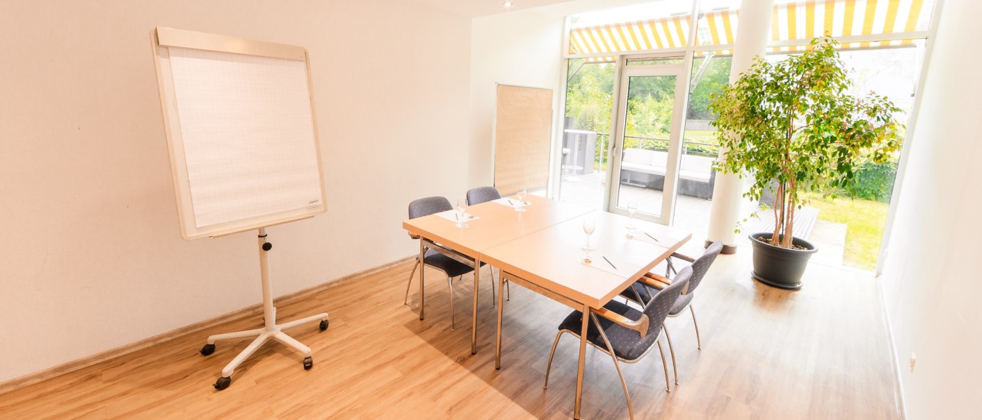 Ein heller Tagungsraum mit einem Tisch, umgeben von Stühlen. Ein Flipchart steht bereit, und eine große Pflanze schmückt den Raum. Fenster bieten Blick ins Grüne., © PLAZA Hotelgroup GmbH Ein heller Tagungsraum mit einem Tisch, umgeben von Stühlen. Ein Flipchart steht bereit, und eine große Pflanze schmückt den Raum. Fenster bieten Blick ins Grüne., © PLAZA Hotelgroup GmbH