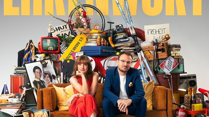 Zwei Personen sitzen auf einem Sofa vor einem chaotischen Haufen aus Alltagsgegenst&auml;nden. Der Schriftzug 'EHRENWORT' ist prominent im Hintergrund zu sehen., &copy; Scala Kultur Live gGmbH