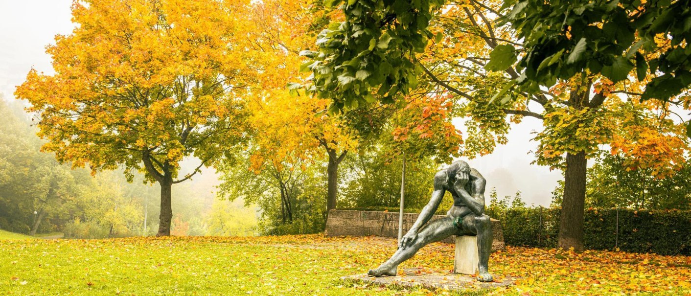 Herbstliche Szene im Stadtpark Leonberg mit einer Skulptur eines nachdenklichen Mannes, umgeben von Bäumen mit gelben und grünen Blättern., © Stuttgart-Marketing GmbH, Sarah Schmid Herbstliche Szene im Stadtpark Leonberg mit einer Skulptur eines nachdenklichen Mannes, umgeben von Bäumen mit gelben und grünen Blättern., © Stuttgart-Marketing GmbH, Sarah Schmid