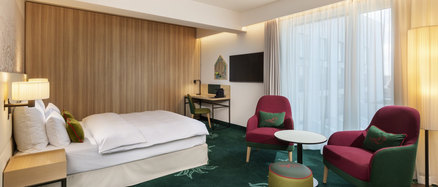 Modernes Hotelzimmer mit Einzelbett, roten Sesseln, Schreibtisch und Fernseher. Grüner Teppichboden und helle Vorhänge sorgen für eine gemütliche Atmosphäre., © Mövenpick Hotel Stuttgart Messe & Congress Modernes Hotelzimmer mit Einzelbett, roten Sesseln, Schreibtisch und Fernseher. Grüner Teppichboden und helle Vorhänge sorgen für eine gemütliche Atmosphäre., © Mövenpick Hotel Stuttgart Messe & Congress