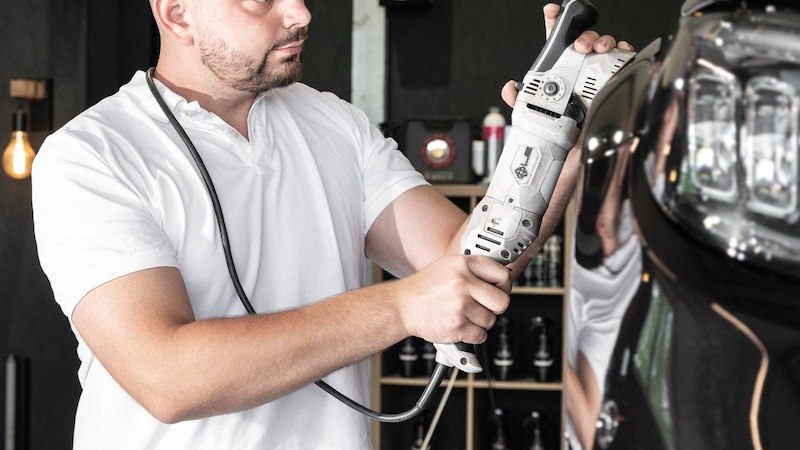 Ein Mann in wei&szlig;em Shirt poliert ein schwarzes Auto mit einer Poliermaschine in einer Werkstatt. Er tr&auml;gt ein Stirnlicht f&uuml;r bessere Sicht., &copy; Mercedes-Benz AG