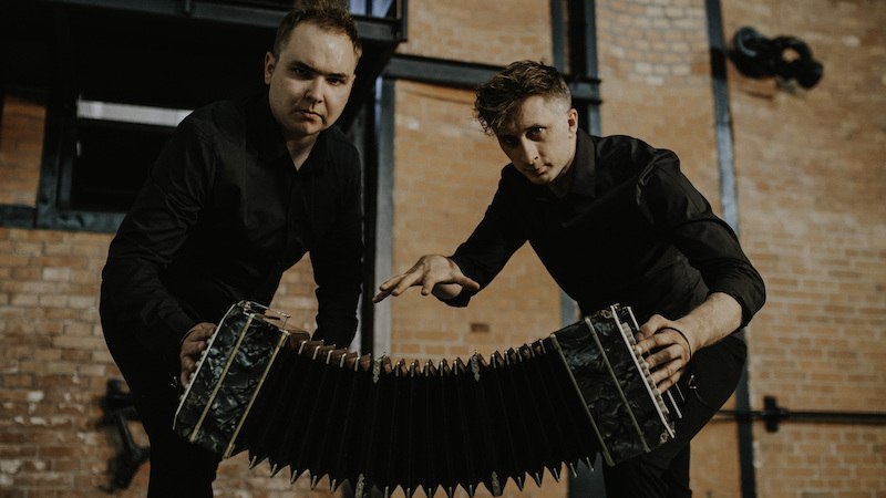 Zwei Männer in schwarzer Kleidung spielen ein Akkordeon vor einer Backsteinwand. Sie schauen ernst in die Kamera., © Stadt Winnenden Zwei Männer in schwarzer Kleidung spielen ein Akkordeon vor einer Backsteinwand. Sie schauen ernst in die Kamera., © Stadt Winnenden