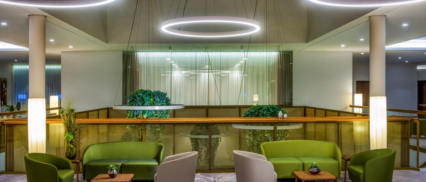 Moderne Lounge mit grünen und beigen Sesseln, runden Tischen und großen, runden Deckenleuchten. Pflanzen und Teppich mit floralem Muster., © Mövenpick Hotel Stuttgart Messe & Congress Moderne Lounge mit grünen und beigen Sesseln, runden Tischen und großen, runden Deckenleuchten. Pflanzen und Teppich mit floralem Muster., © Mövenpick Hotel Stuttgart Messe & Congress