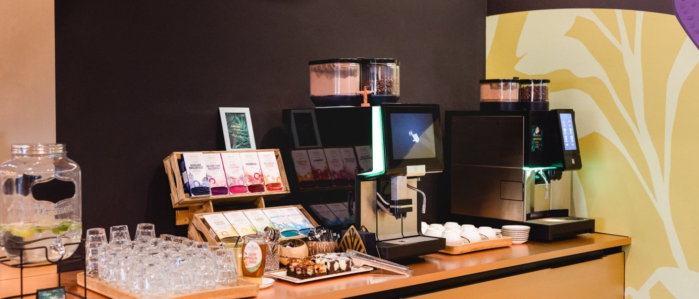 Selbstbedienungsbereich mit Kaffeemaschine, Teesortiment, Gläsern und Snacks auf einem Tresen., © TOMAS Selbstbedienungsbereich mit Kaffeemaschine, Teesortiment, Gläsern und Snacks auf einem Tresen., © TOMAS