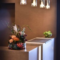 Elegante Rezeption mit Blumenarrangement und modernen Hängelampen. Im Hintergrund eine Schale mit grünen Äpfeln., © TOMAS