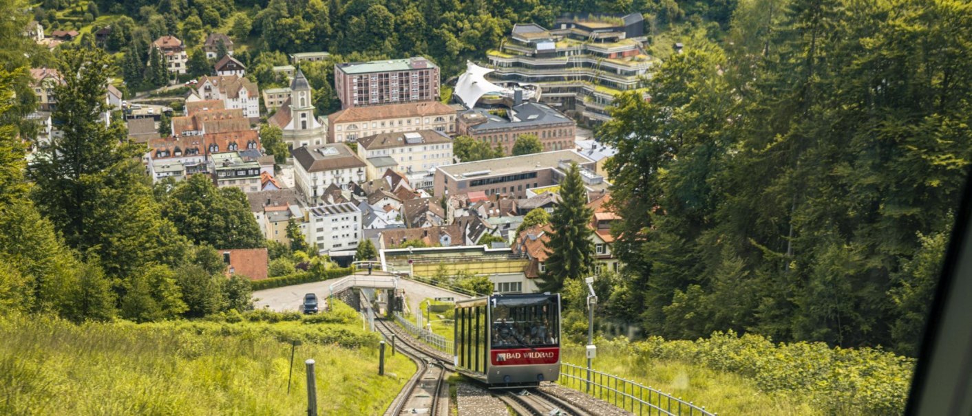 Die Sommerbergbahn in Bad Wildbad fährt durch eine grüne Landschaft mit Blick auf die Stadt im Hintergrund., © Stuttgart-Marketing GmbH, Sarah Schmid Die Sommerbergbahn in Bad Wildbad fährt durch eine grüne Landschaft mit Blick auf die Stadt im Hintergrund., © Stuttgart-Marketing GmbH, Sarah Schmid