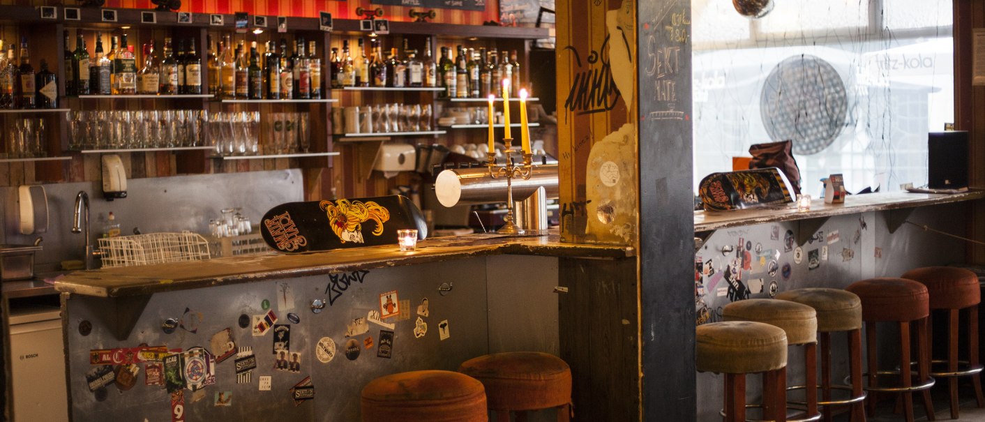 Eine gemütliche Bar mit Skateboard-Dekor auf der Theke, Kerzenleuchter und Barhockern. Im Hintergrund sind Flaschen und Gläser zu sehen., © Mata Hari, Stuttgart
