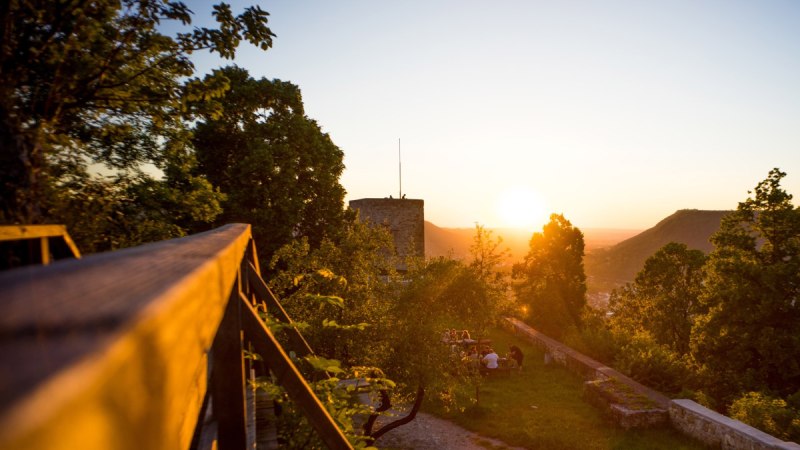 Sonnenuntergang bei der Burgruine Helfenstein. Im Vordergrund sind Bäume und eine Gruppe von Menschen zu sehen, die die Aussicht genießen., © Landkreis Göppingen
