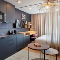 Modernes Studio mit dunkler Küche, Schreibtisch, Bett und stilvoller Beleuchtung. Vorhänge trennen den Schlafbereich ab., © Adagio