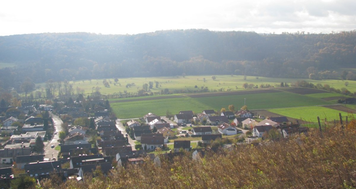 Ein Dorf in einer gr&uuml;nen Landschaft, umgeben von Feldern und H&uuml;geln unter einem bew&ouml;lkten Himmel., &copy; Land der 1000 H&uuml;gel - Kraichgau-Stromberg