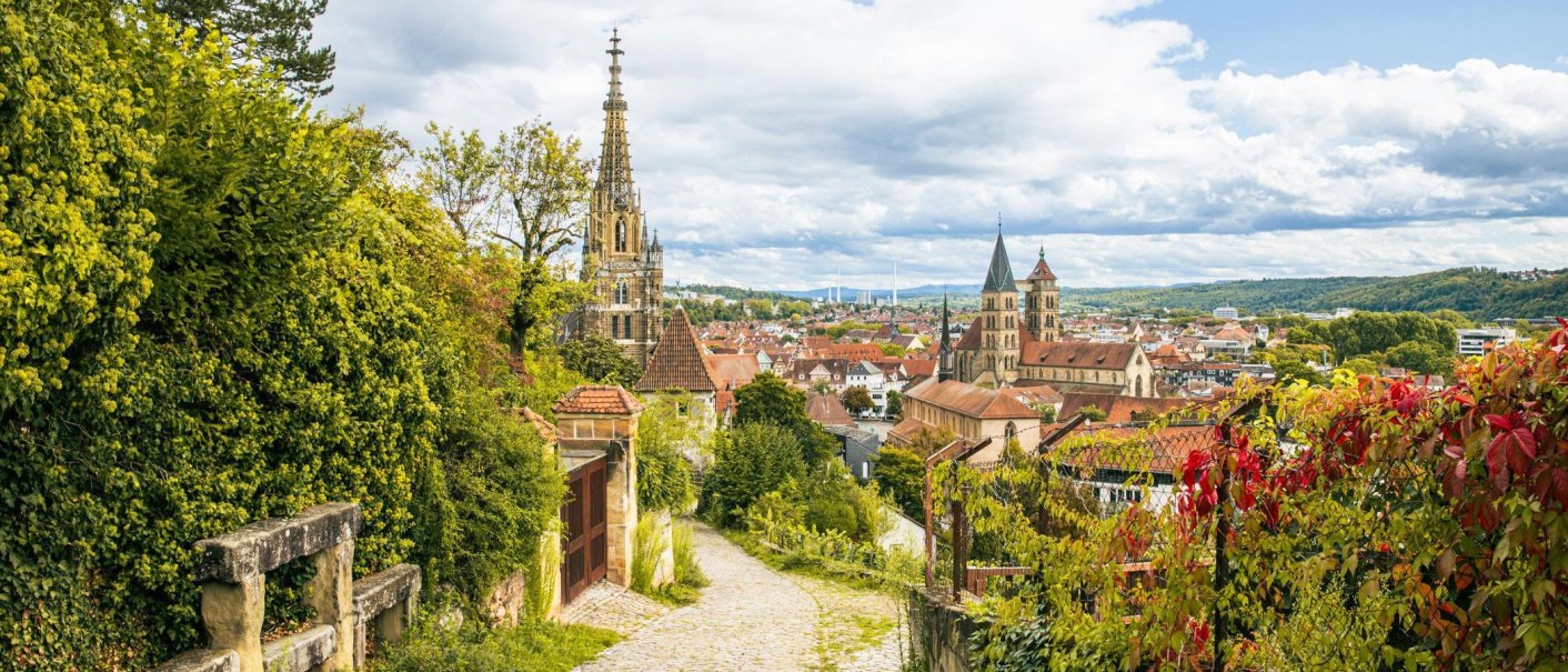Panoramablick auf Esslingen mit Weinbergen, historischen Gebäuden und einer Kirche im Hintergrund. Üppige Vegetation und ein gepflasterter Weg im Vordergrund., © Stuttgart-Marketing GmbH, Sarah Schmid Panoramablick auf Esslingen mit Weinbergen, historischen Gebäuden und einer Kirche im Hintergrund. Üppige Vegetation und ein gepflasterter Weg im Vordergrund., © Stuttgart-Marketing GmbH, Sarah Schmid