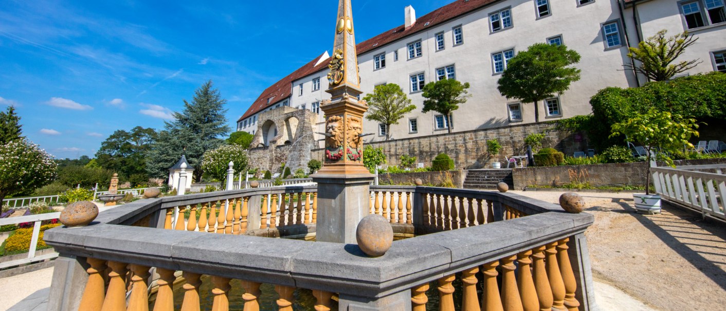 Schloss Leonberg mit Pomeranzengarten. Ein Obelisk steht im Vordergrund, umgeben von gepflegten Gärten und Bäumen unter blauem Himmel., © SMG Achim Mende Schloss Leonberg mit Pomeranzengarten. Ein Obelisk steht im Vordergrund, umgeben von gepflegten Gärten und Bäumen unter blauem Himmel., © SMG Achim Mende