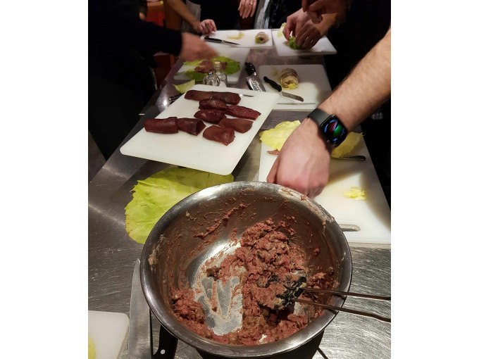 Teilnehmer eines Kochkurses bereiten Fleisch und Zutaten auf Schneidebrettern vor. Eine Schüssel mit Fleischmasse steht im Vordergrund., © Kultweine-Kochwelten-Kunstücke - Kochschule Sonja Lenz Teilnehmer eines Kochkurses bereiten Fleisch und Zutaten auf Schneidebrettern vor. Eine Schüssel mit Fleischmasse steht im Vordergrund., © Kultweine-Kochwelten-Kunstücke - Kochschule Sonja Lenz