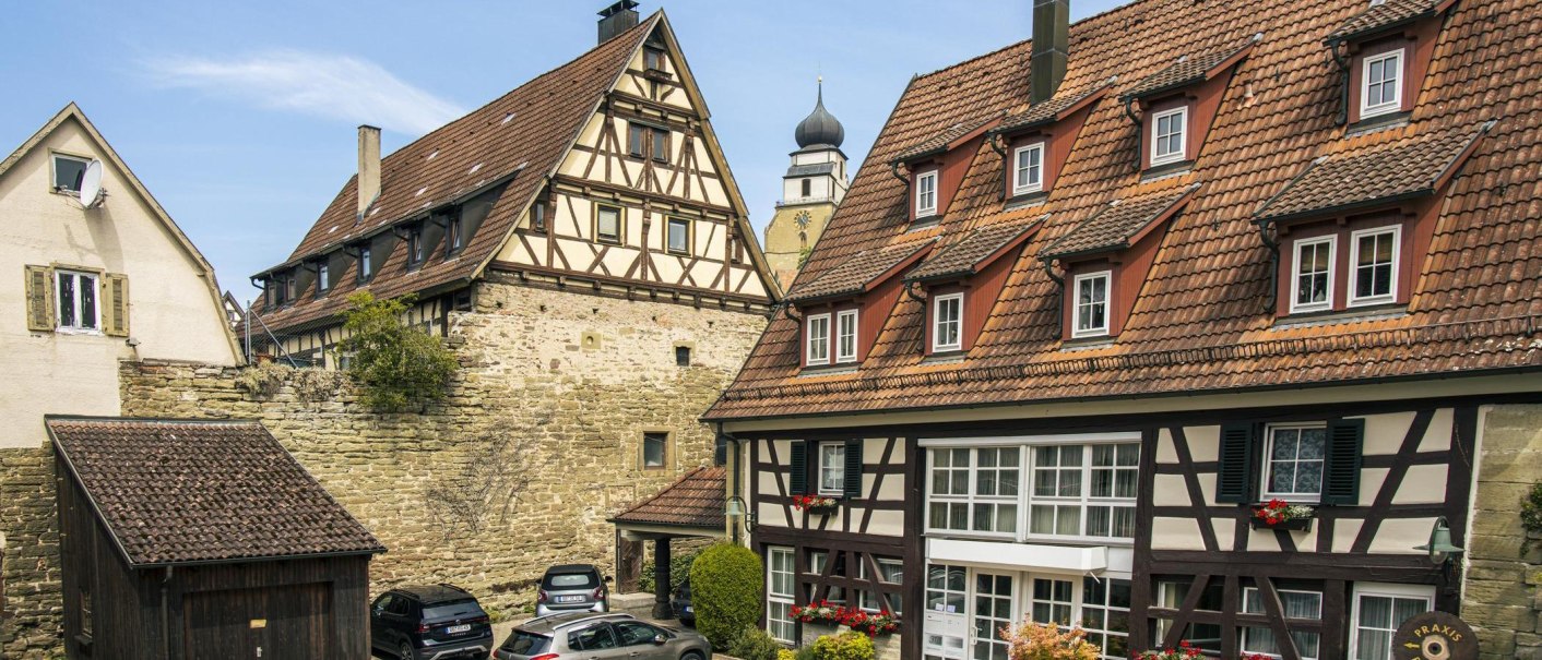 Fachwerkhäuser in der Altstadt von Herrenberg, Deutschland. Im Hintergrund ist ein Kirchturm zu sehen. Die Gebäude haben rote Ziegeldächer und blühende Blumenkästen., © SMG, Sarah Schmid Fachwerkhäuser in der Altstadt von Herrenberg, Deutschland. Im Hintergrund ist ein Kirchturm zu sehen. Die Gebäude haben rote Ziegeldächer und blühende Blumenkästen., © SMG, Sarah Schmid