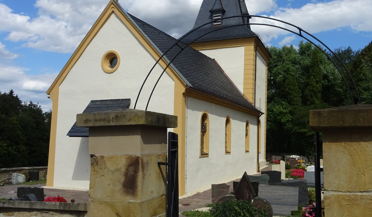 Die Ottilienkirche Bettringen mit gelben Akzenten, umgeben von einem Friedhof, unter einem blauen Himmel mit weißen Wolken., © Foto: Cornelia Steinbach Die Ottilienkirche Bettringen mit gelben Akzenten, umgeben von einem Friedhof, unter einem blauen Himmel mit weißen Wolken., © Foto: Cornelia Steinbach