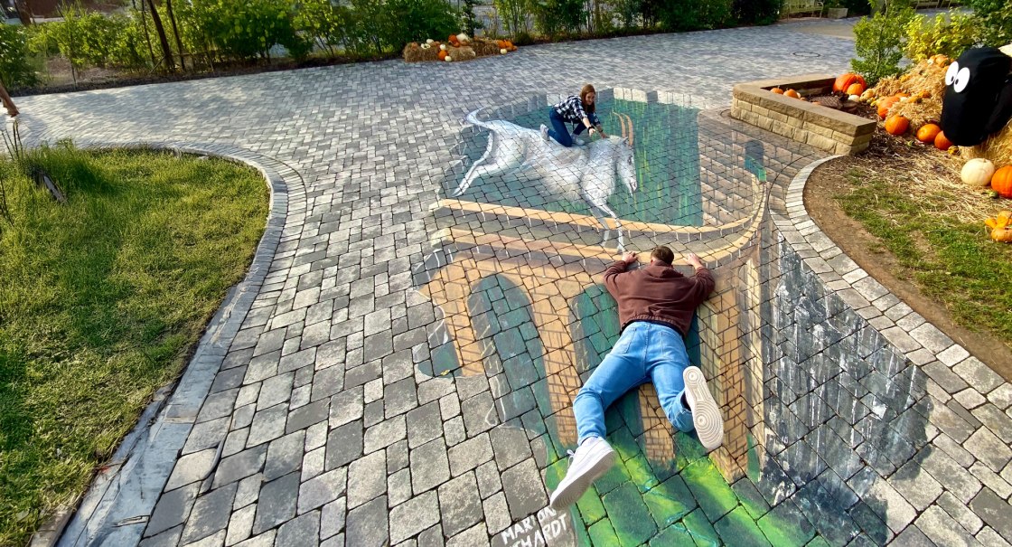 Zwei Personen posieren auf einer 3D-Stra&szlig;enmalerei, die eine Br&uuml;cke und ein Einhorn zeigt. Die Illusion wirkt realistisch auf dem gepflasterten Boden., &copy; Erlebnispark Tripsdrill