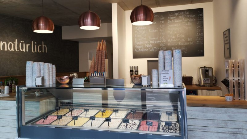 Eisdiele mit Eistheke, verschiedenen Eissorten, Menütafel und moderner Beleuchtung. Schriftzug 'natürlich' an der Wand., © Joannis Nakos Eisdiele mit Eistheke, verschiedenen Eissorten, Menütafel und moderner Beleuchtung. Schriftzug 'natürlich' an der Wand., © Joannis Nakos