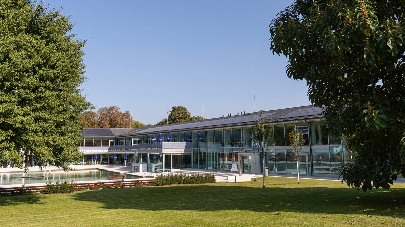 Das Bild zeigt den Außenbereich des Mineralbads Berg mit einem Pool, umgeben von modernen Gebäuden und grünen Bäumen unter klarem Himmel., © Stuttgarter Bäder