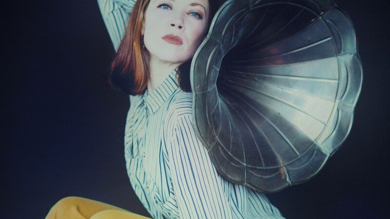 Frau in gestreiftem Hemd und gelber Hose posiert mit einem Grammophontrichter vor dunklem Hintergrund., © Mauerwerk GmbH