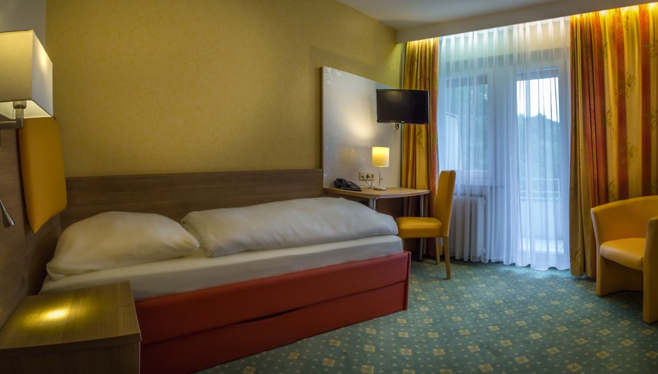 Ein gemütliches Einzelzimmer mit Bett, Schreibtisch, Stuhl und Fernseher. Gelbe Vorhänge und Teppich sorgen für eine warme Atmosphäre., © Kulinarium an der Glems