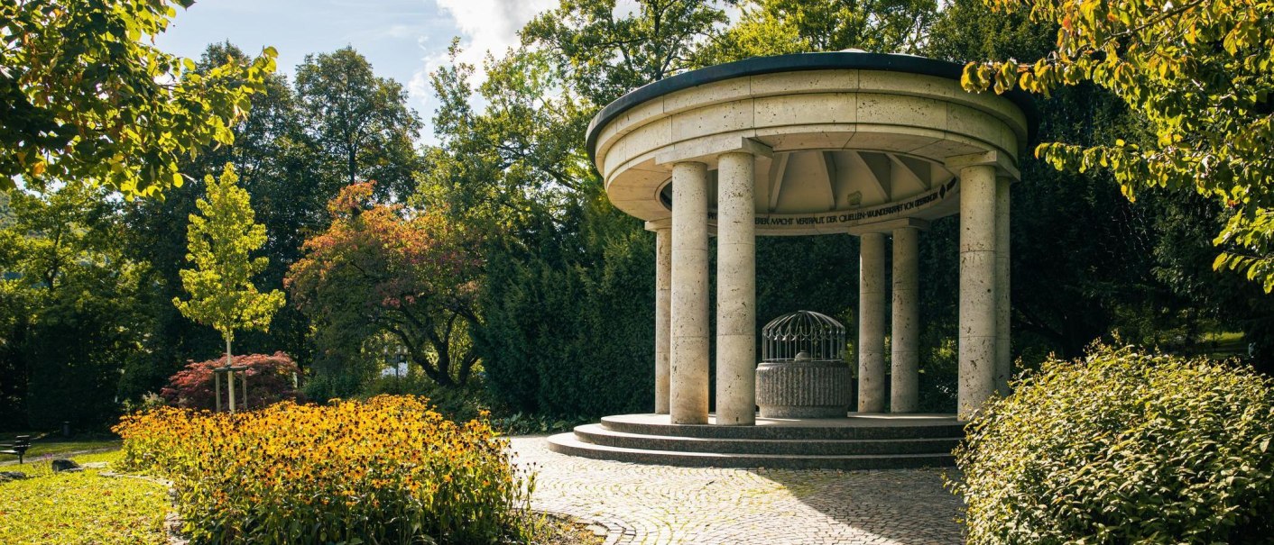 Ein runder Pavillon mit Säulen im Grünen, umgeben von Bäumen und blühenden Pflanzen. Der Himmel ist klar und sonnig., © SMG, Sarah Schmid Ein runder Pavillon mit Säulen im Grünen, umgeben von Bäumen und blühenden Pflanzen. Der Himmel ist klar und sonnig., © SMG, Sarah Schmid