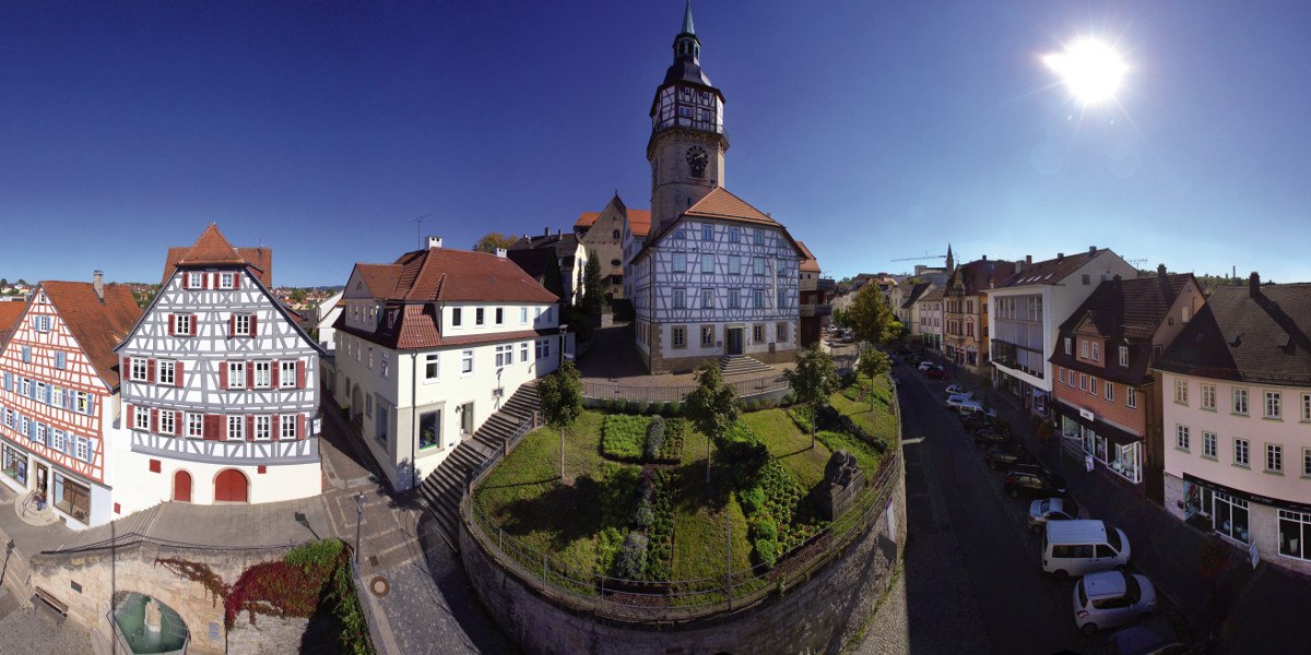 Panorama von Backnang mit Fachwerkhäusern, einem Kirchturm und blühenden Gärten unter strahlend blauem Himmel und Sonnenschein., © Stuttgart-Marketing GmbH