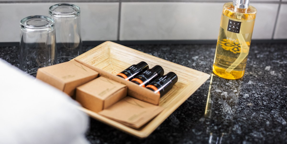 Hotel-Badezimmer mit Pflegeprodukten auf einem Tablett, zwei Gläsern und einem Rituals Infinity Seifenspender auf einer Granitoberfläche., © Kronen Hotel GmbH